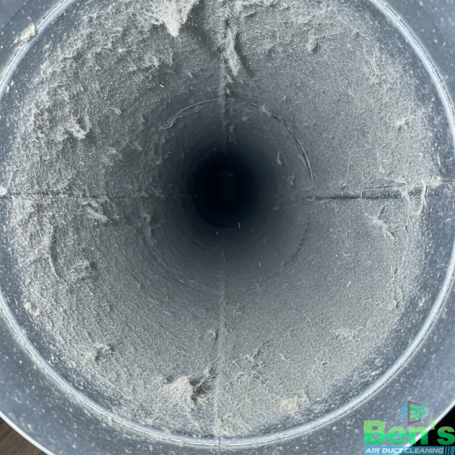 Looking down the inside of a residential air duct before cleaning — walls coated in grey dust and lint